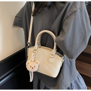 Crocodile pattern cream bucket bag with pink bear charm shown in a side-carry style