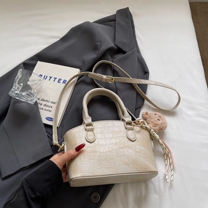 Detailed macro of cream faux crocodile bucket bag with plush bear charm and woven cord