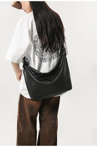 Detail of a large black tote bag with textured synthetic leather and wide shoulder strap