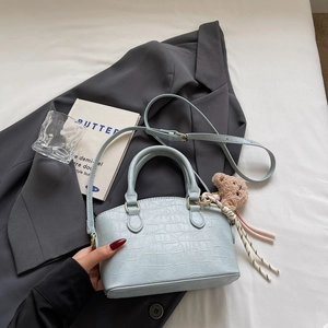 Top-down view of a light blue croc-embossed shell handbag with cute bear charm and strap
