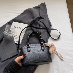Detail of black crocodile pattern bucket bag with bear charm on grey blazer backdrop