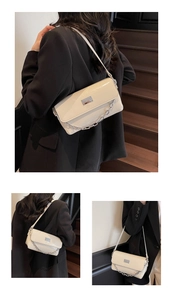 Detail of a creamy white baguette bag with silver metal chain and glossy leather texture