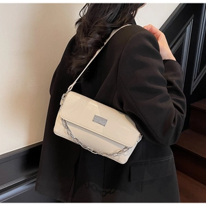 Detail shot of chic beige chain baguette bag with glossy finish on shoulder
