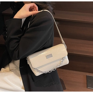 Detail of a creamy white patent leather baguette bag with silver chain and metal plaque