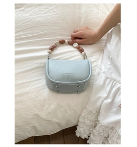 Detail of light blue bucket bag with decorative marble beaded handle on fabric