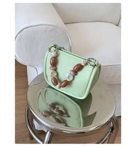 Detail of mint green pebble grain leather bucket bag with marble resin chain on metal stool