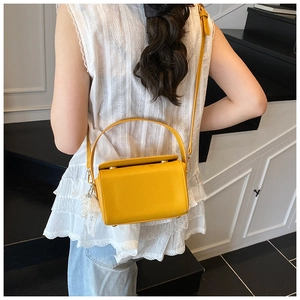 Détail d'un sac boîte en cuir jaune avec pendentif en dentelle porté par un mannequin