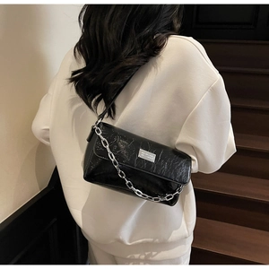 Detail of black glossy pleated crossbody bag with thick silver chain and metal buckle