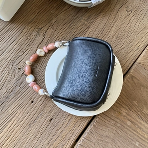 Detail of black lychee grain leather bucket bag featuring pink and white beaded handle