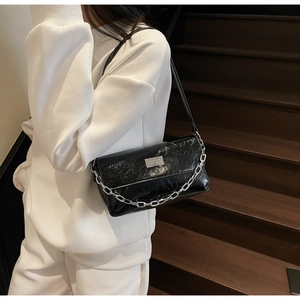 Detail of glossy black pleated underarm bag with silver chain and metal logo plate