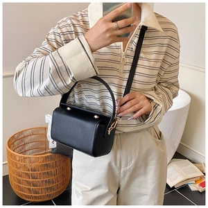 Détail d'un sac boîte en cuir noir avec ferrures dorées porté sur un haut rayé