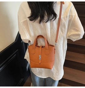 Detail view of an orange-brown pebble leather bucket bag with silver twist lock and strap