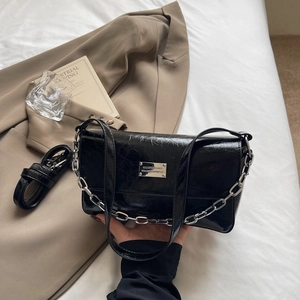 Detail of black glossy oil wax leather bag with silver chain and metal nameplate