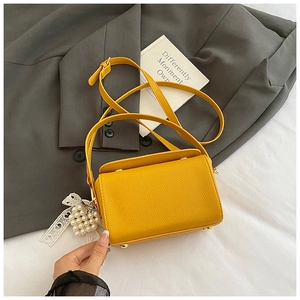 Vue détaillée du sac boîte jaune en cuir texturé avec breloque en perles et ruban