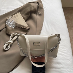 Detail of off-white glossy faux leather bag with silver chain strap and metal logo