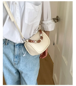 Detail of creamy white bucket bag with elegant marbled beaded handle and pebble leather texture