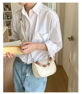 Close-up of cream bucket bag with unique brown marble bead chain handle and leather strap