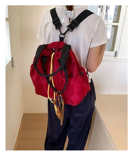 Detail of red nylon drawstring backpack featuring black wide straps and decorative charms