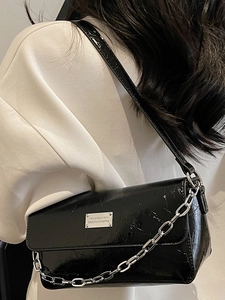 Modern black glossy baguette bag with silver chain and metal plaque on shoulder