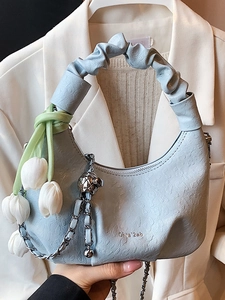 Sac dumpling bleu clair avec chaîne et breloque fleur, présenté en tenue élégante