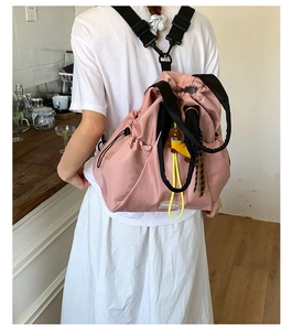 Detail of pink nylon backpack featuring black webbing straps and yellow drawstring accents