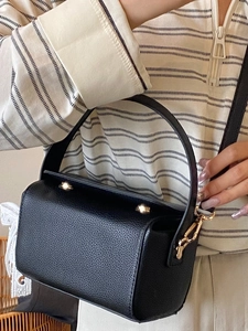 Sac boîte minimaliste en cuir grainé noir avec boucles dorées porté par un mannequin
