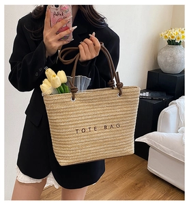Detail of woven straw tote bag featuring black TOTE BAG print and brown leather handles