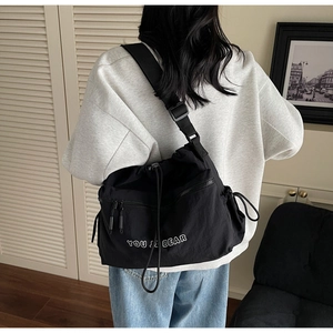Back view of a model wearing a large black nylon messenger bag with drawstring closure