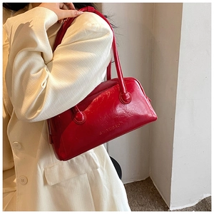 Close-up of red patent leather Boston bag with embossed logo and sleek shoulder straps