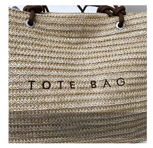 Close-up of woven straw tote bag with TOTE BAG embroidery and knotted rope handle detail