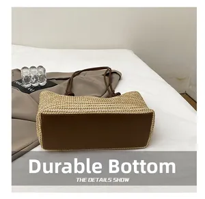 Detail showing the wear-resistant reinforced brown bottom of the straw tote bag