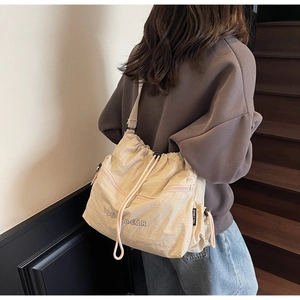 Detail of the drawstring closure and embroidered texture on the beige shoulder bag