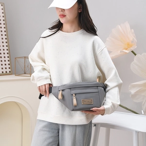 Détail du sac banane en nylon gris avec étiquette de marque et tirette de zip en cuir