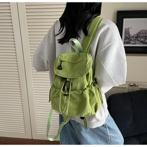 Green drawstring backpack in wrinkled nylon fabric worn by a person in a modern interior