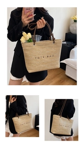 Detailed macro view of woven straw tote bag with black embroidery and brown handles