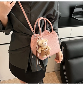 Détail d'un sac à main rose en cuir grainé avec poignées rondes et pendentif ours mignon