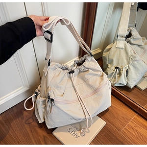 Detail view of beige nylon crossbody bag with drawstring closure and wide strap