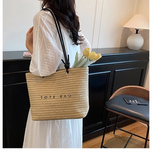 Detail of a beige straw tote bag with black embroidery and rope handles for summer beach