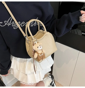 Gros plan du sac seau en cuir grainé crème avec un pendentif ours en peluche