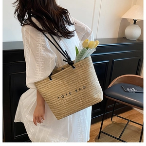 Handwoven straw tote bag with black shoulder straps and TOTE BAG print on the front surface