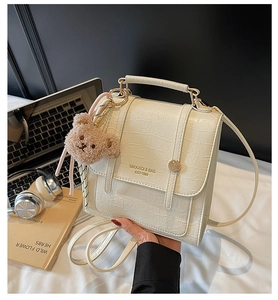 Detail of cream crocodile embossed bag with top handle and brown bear charm on desk