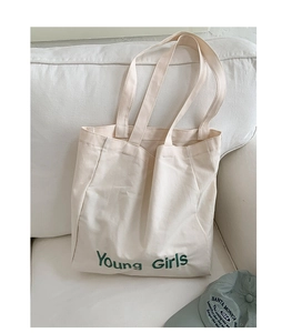 Detailed close-up of cream canvas tote bag with green Young Girls lettering on a sofa
