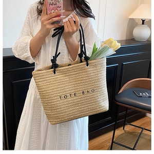 Detail of handwoven beige straw tote bag with black TOTE BAG embroidery and sturdy rope handles