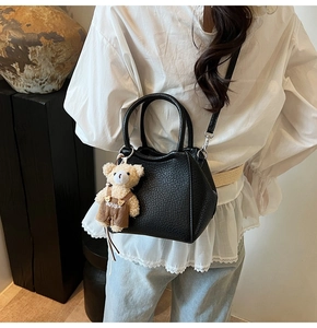 Détail du sac seau noir en cuir grainé avec un charm ours porté par un mannequin