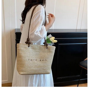 Detail of straw woven tote bag with brown embroidery and knotted faux leather shoulder strap