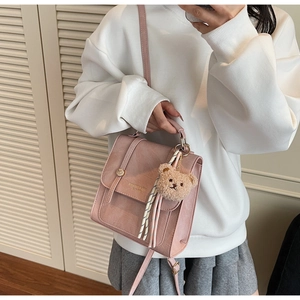 Pink croc-effect crossbody bag featuring a plush bear charm on a white hoodie model