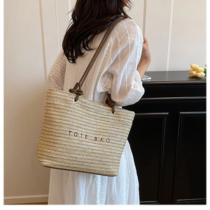 Detailed shot of straw woven tote bag with TOTE BAG embroidery and slim leather handles