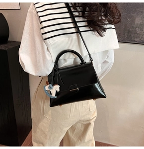 Close-up of black leather tote bag with blue horse charm and gold bottom studs