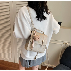 Detail of beige crocodile embossed crossbody bag with gold metal buckle and cute bear charm