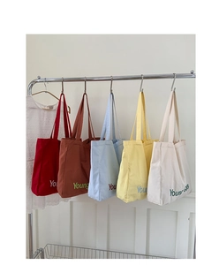 Detail showing five colorful canvas tote bags with contrast letter embroidery hanging on a rack
